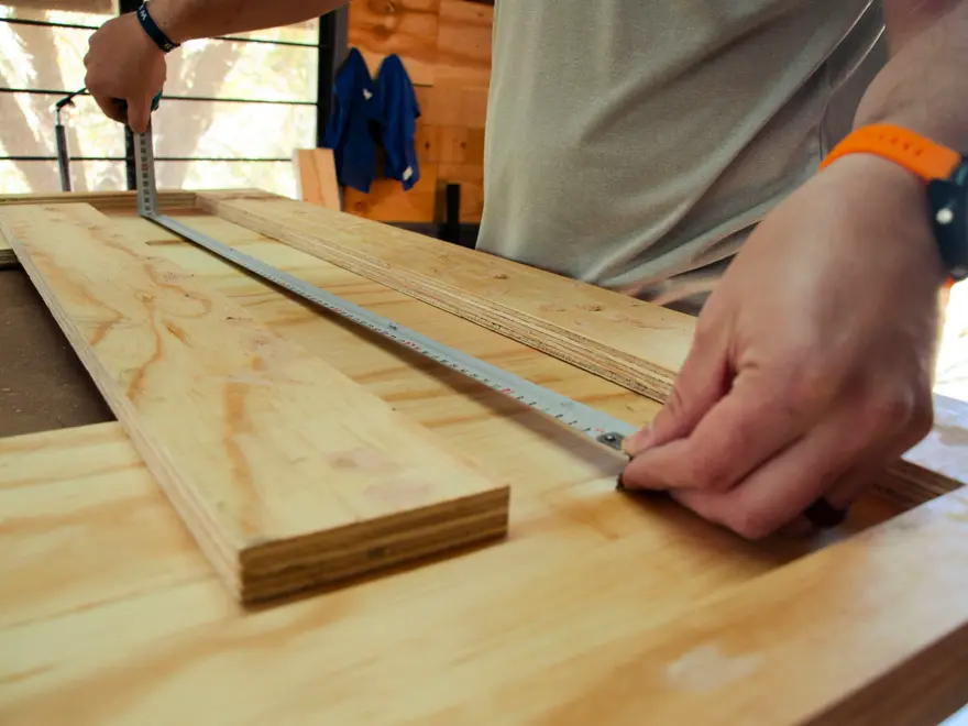Carpenter measuring a plywood panel with a tape measure