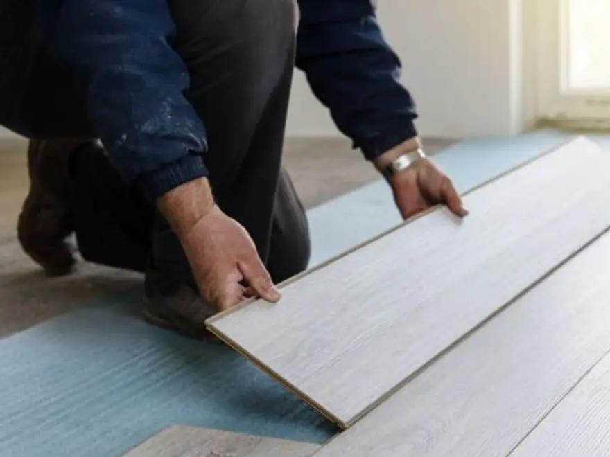 Tradesperson laying a light wood-effect floor plank over underlay