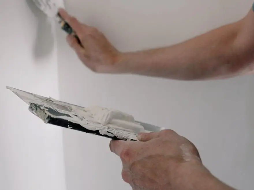 Plasterer applying white plaster to a wall with a trowel
